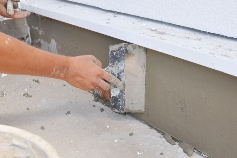A contractor is plastering, repairing stucco house foundation after styrofoam insulation.