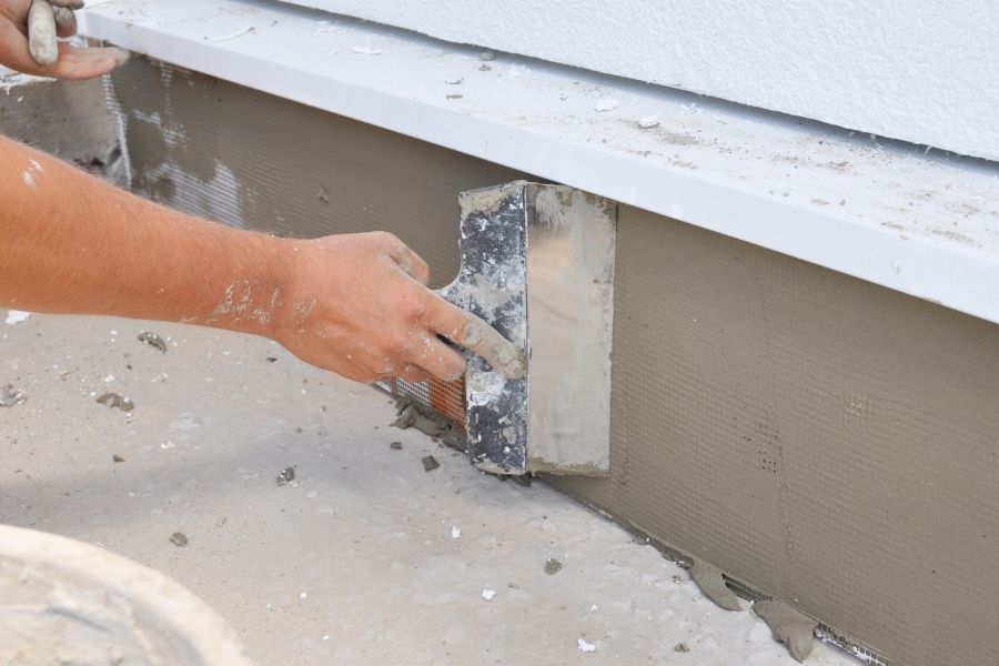 A contractor is plastering, repairing stucco house foundation after styrofoam insulation.
